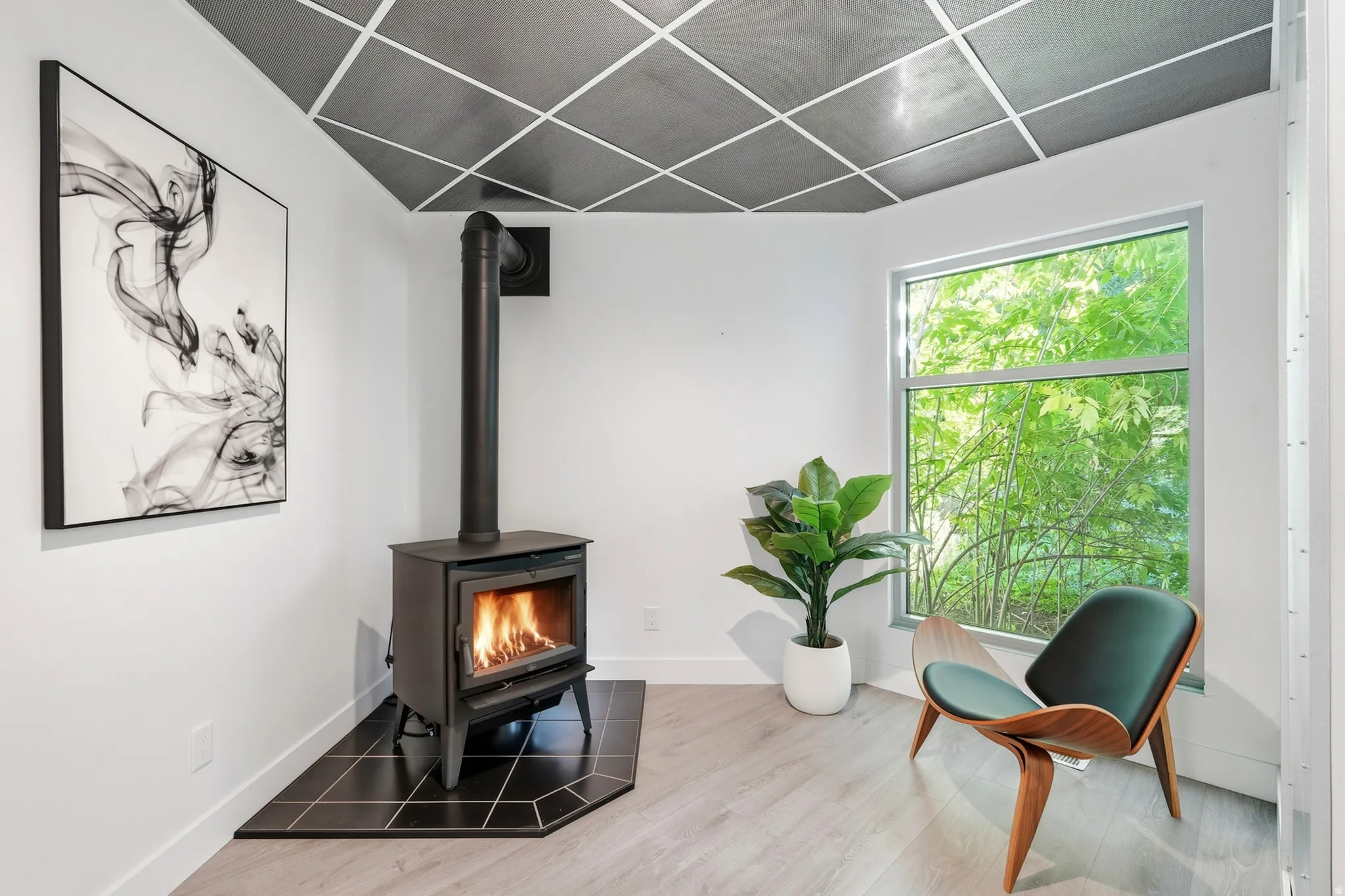 Wood-burning stove with a black tile hearth, wood-finish flooring, and a large window