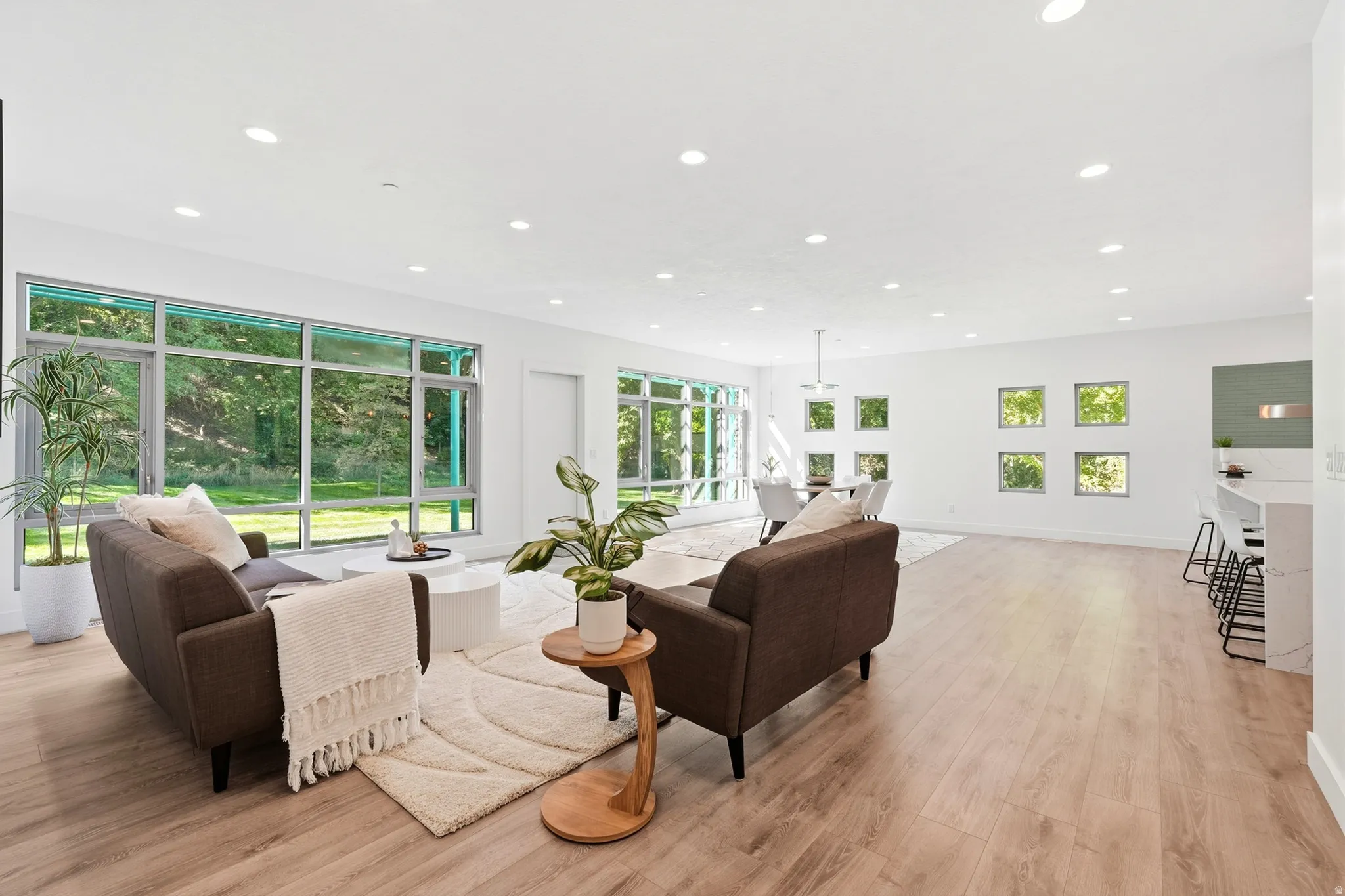 Open-concept living area with light wood-finish flooring, recessed lighting, expansive floor-to-ceiling windows, and white walls