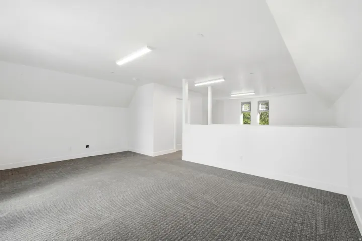 Expansive room featuring clean white walls, grey patterned carpeting, a partial wall, and multiple windows providing natural light