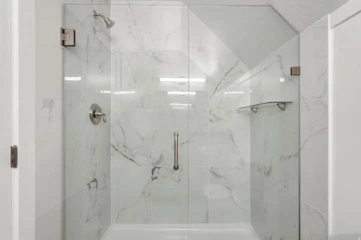 Glass-enclosed shower featuring large format tile, brushed nickel fixtures, a built-in shelf, and a textured ceiling