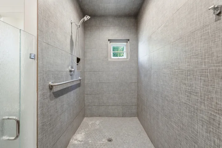 Walk-in shower with textured wall tiles, a built-in window, and a grab bar
