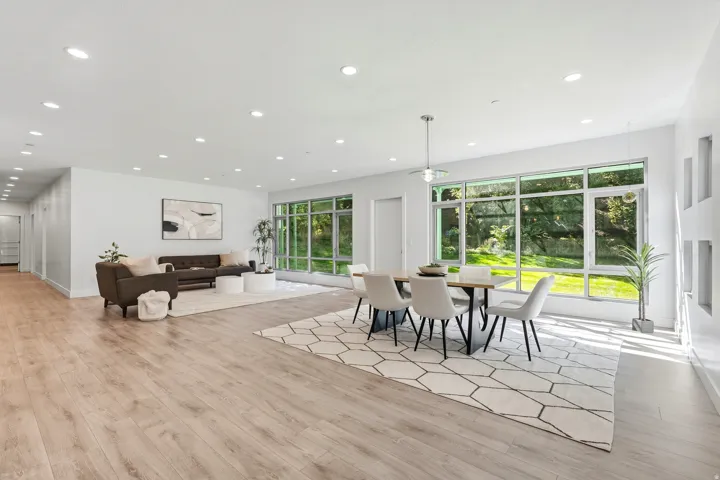 Open-concept living and dining area featuring wood-finish flooring, recessed lighting, and expansive windows