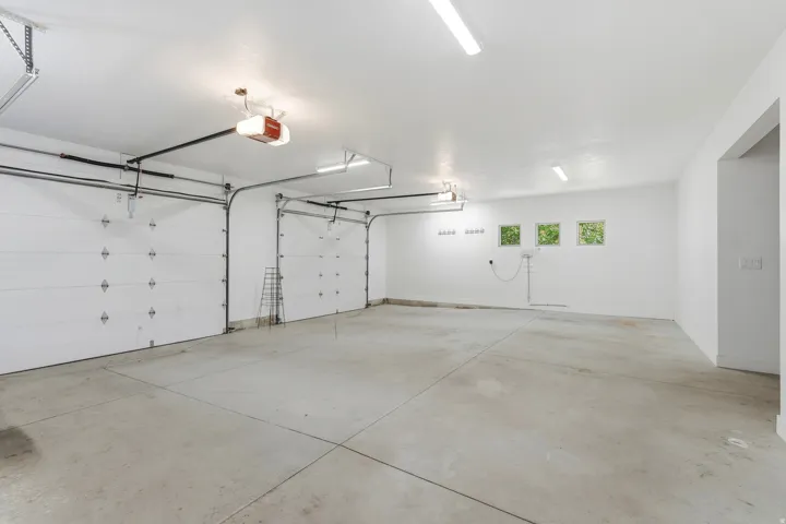 Two overhead garage doors with automatic openers, three transom windows, a concrete floor, and fluorescent ceiling lighting