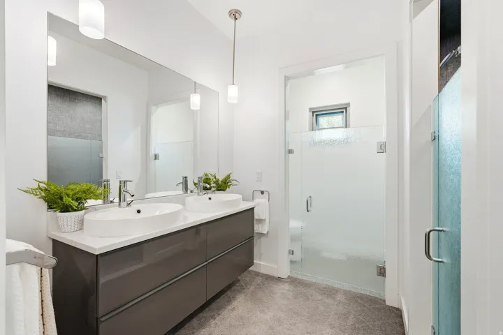 Dual vessel sinks on a spacious vanity, large wall-mounted mirror, modern pendant lighting, and a walk-in shower with frosted glass