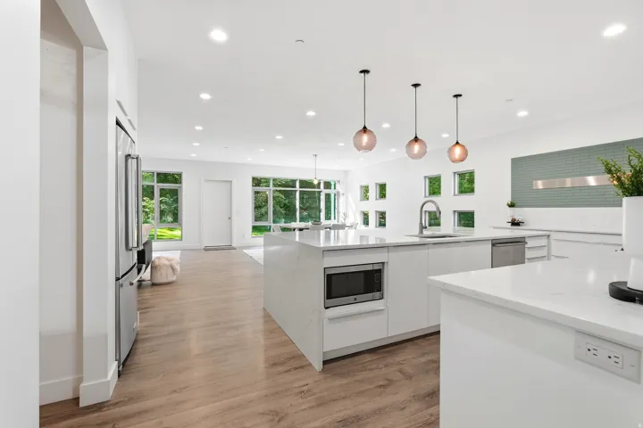 Open-concept kitchen with white cabinetry and countertops, integrated stainless steel appliances, wood-finish flooring, and recessed lighting