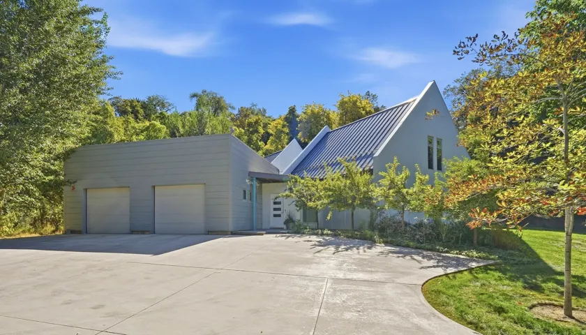 Modern exterior with a striking metal roof, an attached two-car garage, a concrete driveway, and mature perimeter trees