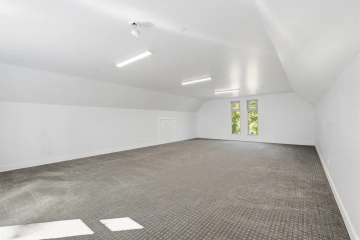 Spacious room featuring vaulted ceilings, recessed windows, wall-to-wall carpeting, and bright overhead lighting