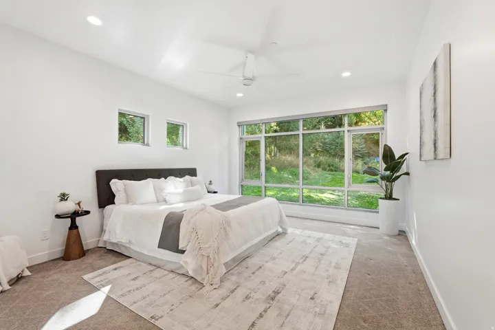 Recessed lighting illuminates the space, featuring a large picture window, two high-set windows, a ceiling fan, and carpeted flooring