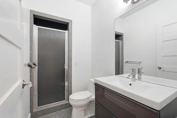 Vanity with integrated sink and chrome faucet, frameless mirror, and stall shower with textured glass door