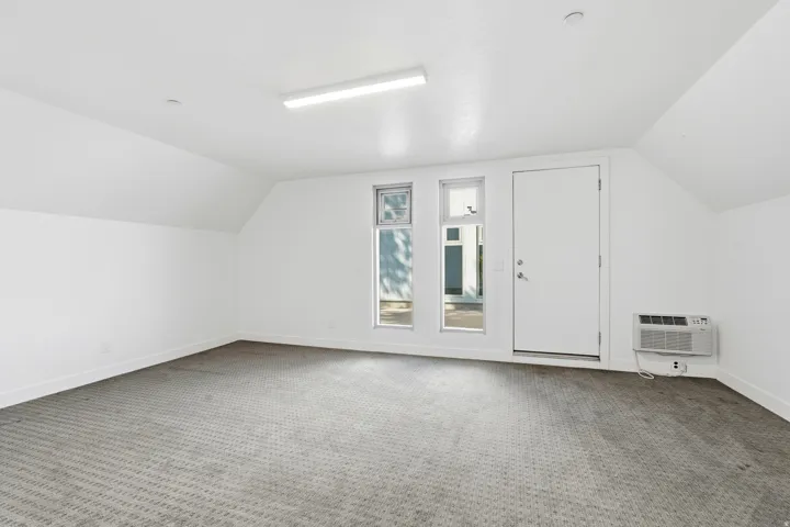 Spacious room featuring textured carpeting, white painted walls, and an angled ceiling