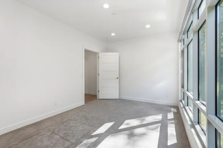 Recessed ceiling lighting, white interior walls, gray carpeting, white paneled door, and expansive window wall