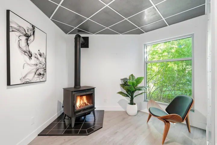 Wood-burning stove with a black tile hearth, wood-finish flooring, and a large window