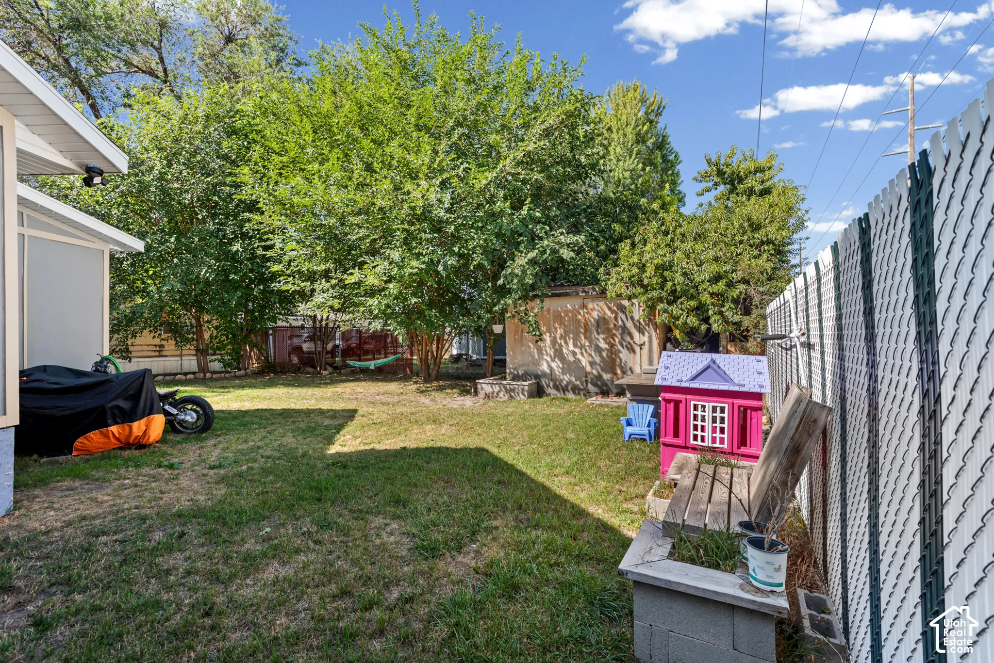 Secluded backyard featuring a chain-link fence, mature trees, and a shed