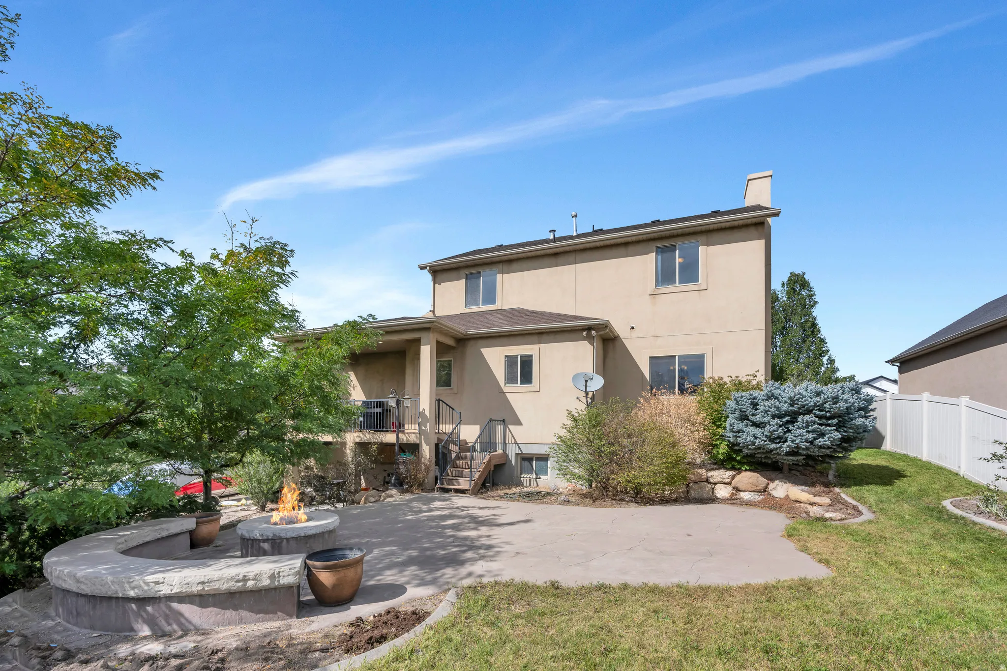 Expansive patio featuring a built-in fire pit, curved stone seating, and mature landscaping