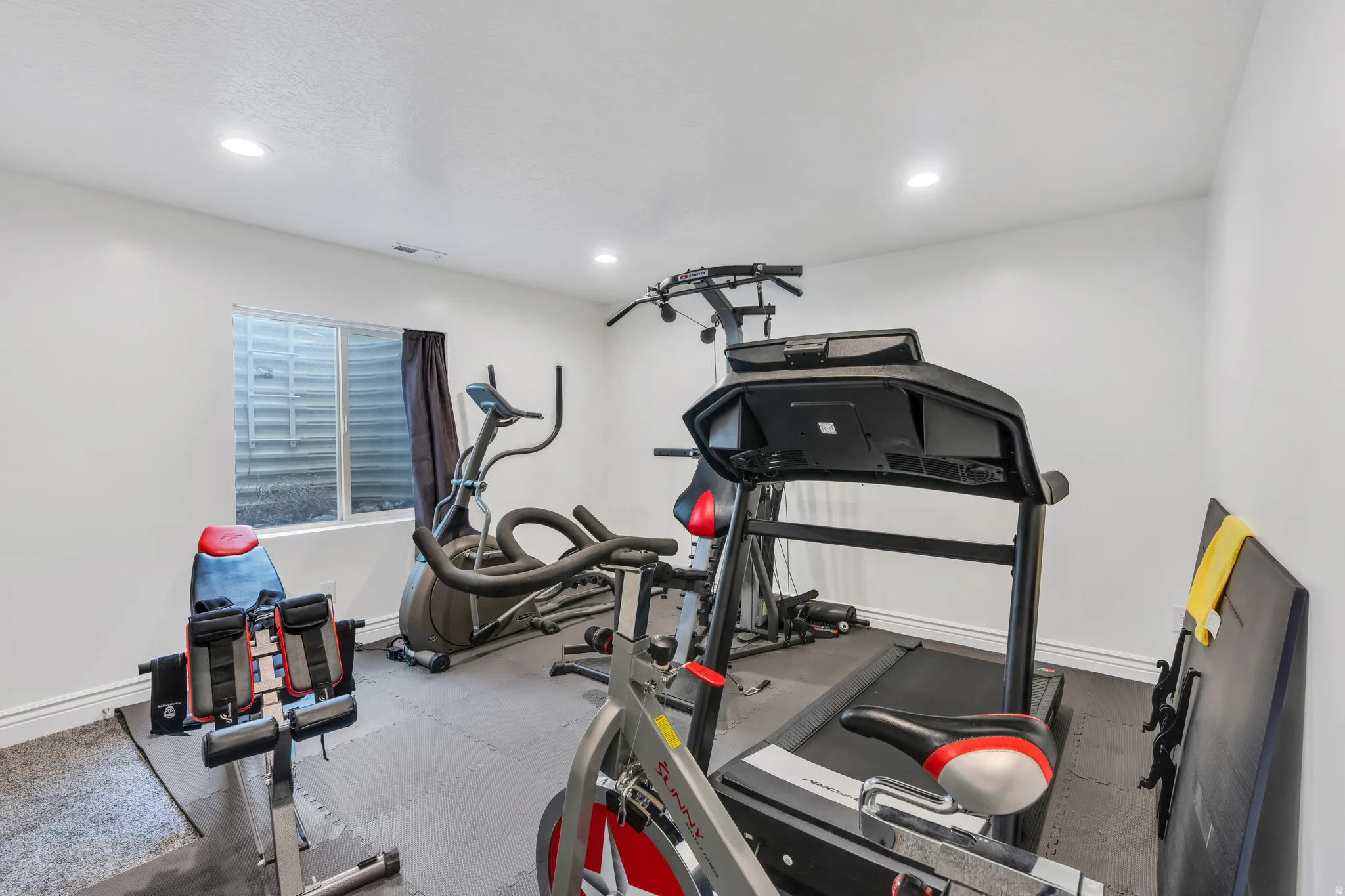 Recessed lighting illuminates a versatile space featuring a window with privacy covering and rubber flooring