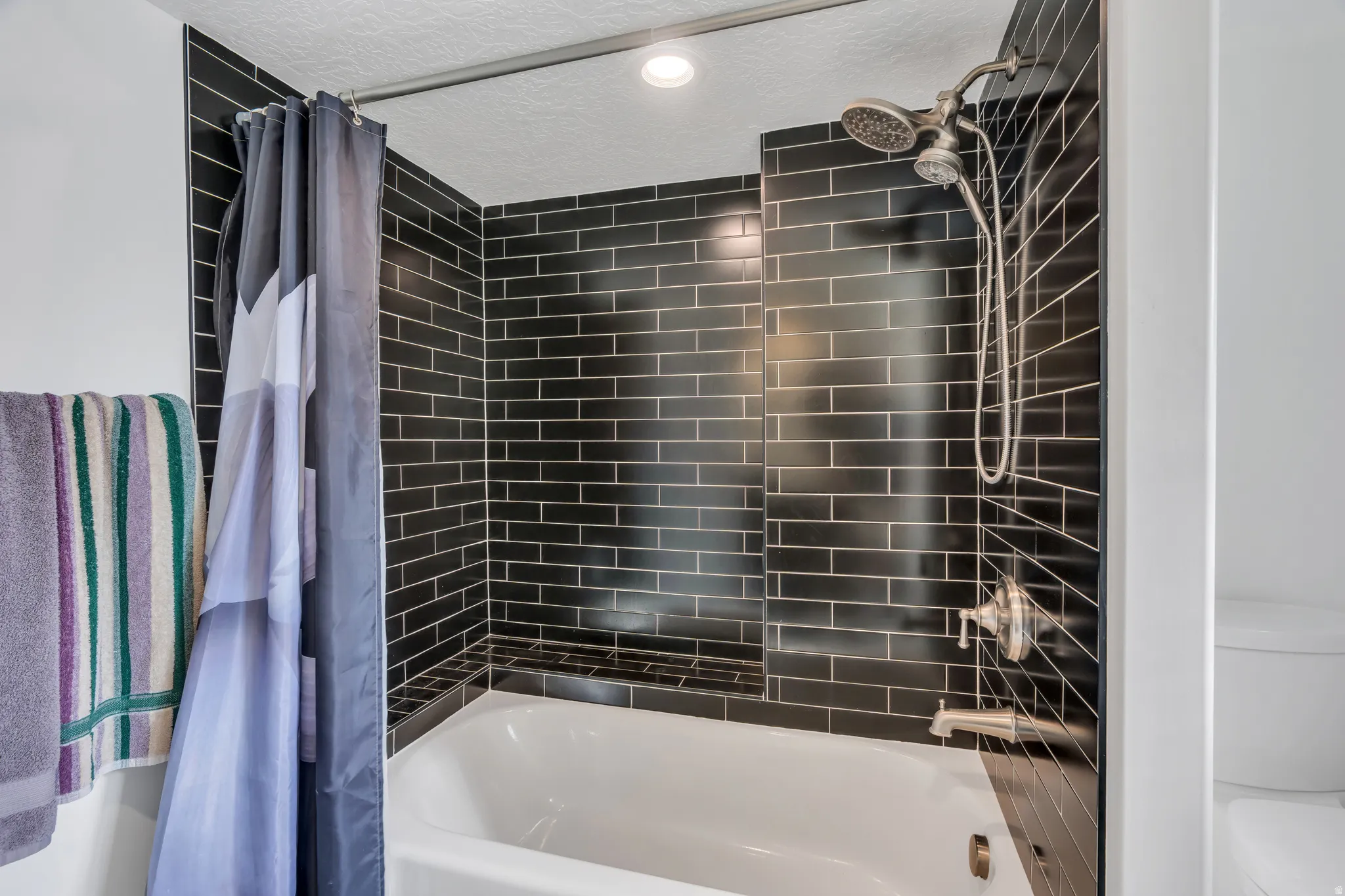 Bathtub with dark subway tile surround, built-in shower niche, and brushed nickel fixtures