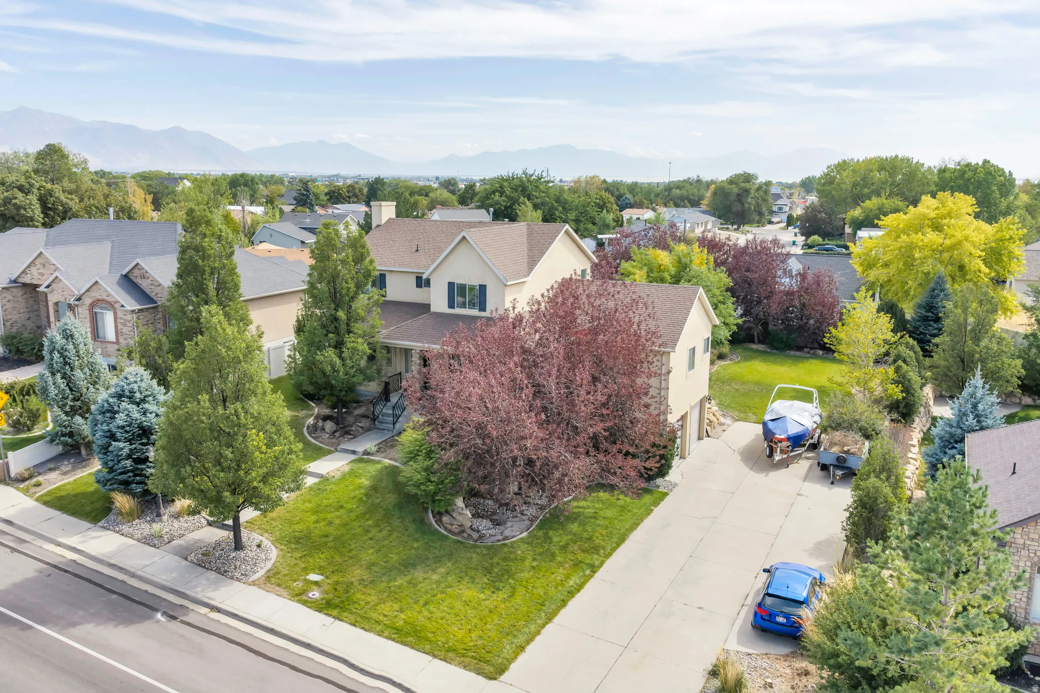 Two-story residence featuring a covered front porch, an attached garage, a paved driveway, and established landscaping with mature trees