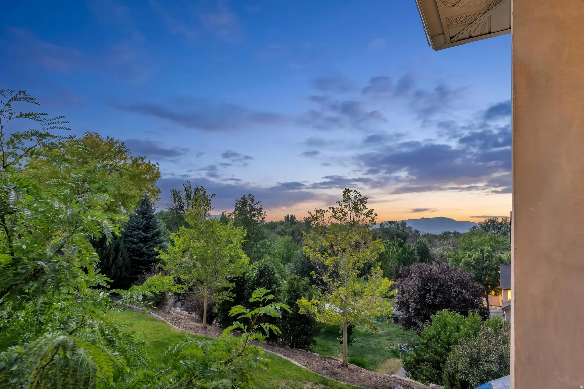 Expansive green landscaping with a variety of mature trees and distant mountain range, sunset views, twilight added