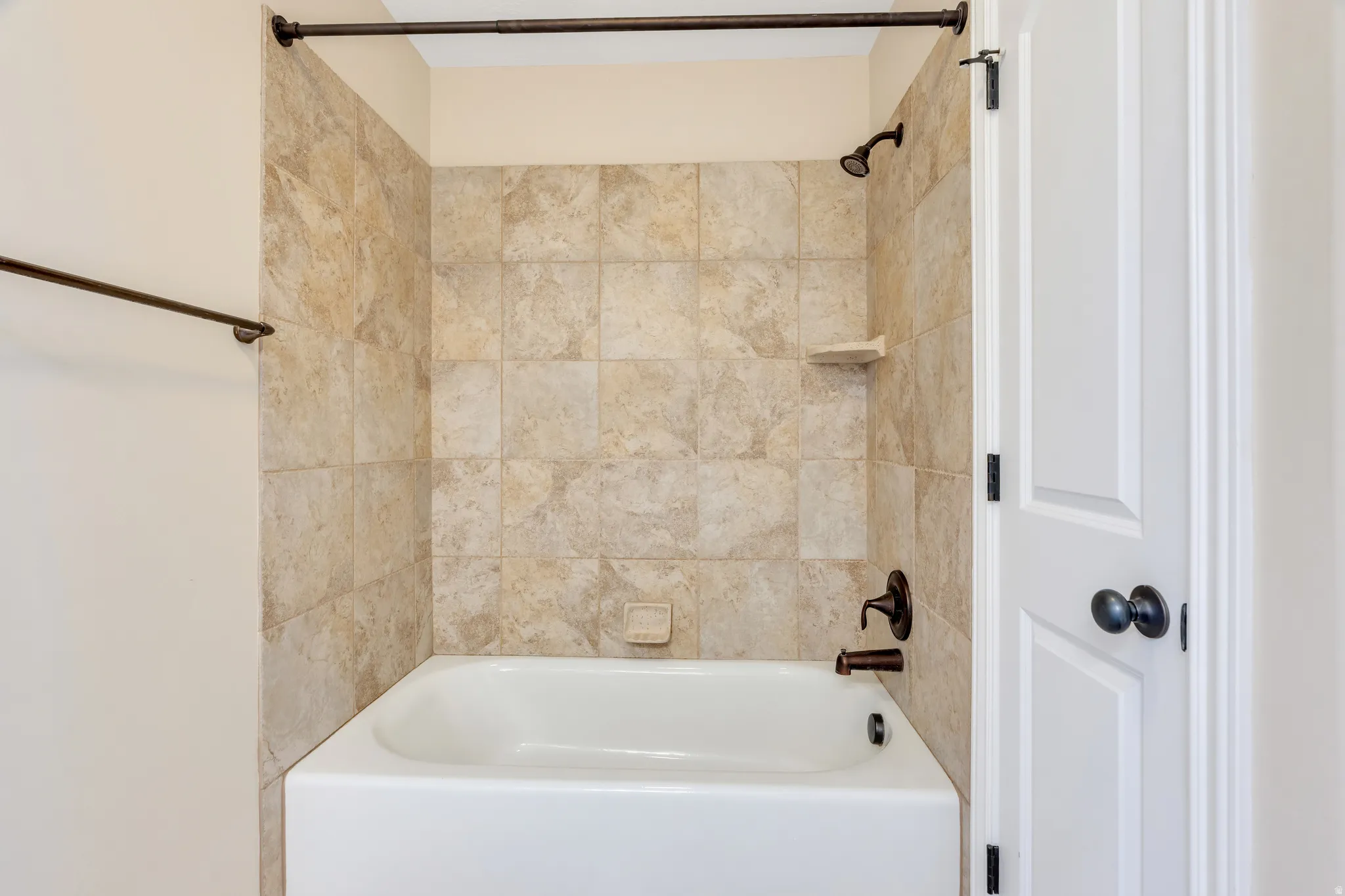 White bathtub featuring tiled surround, bronze-finish fixtures, and a wall-mounted shower head