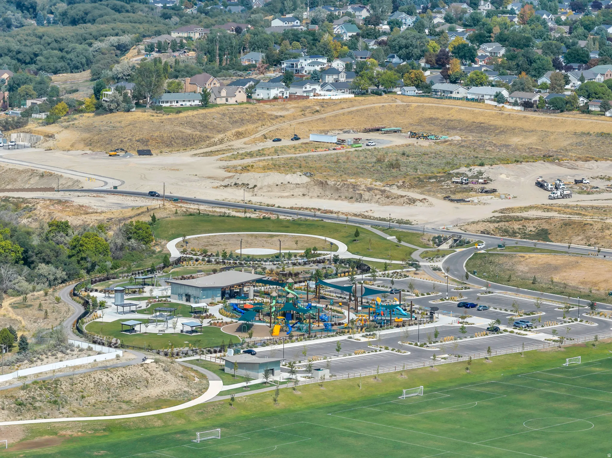 Expansive recreational park featuring a water play area, multiple playground structures, athletic fields, and paved walking paths