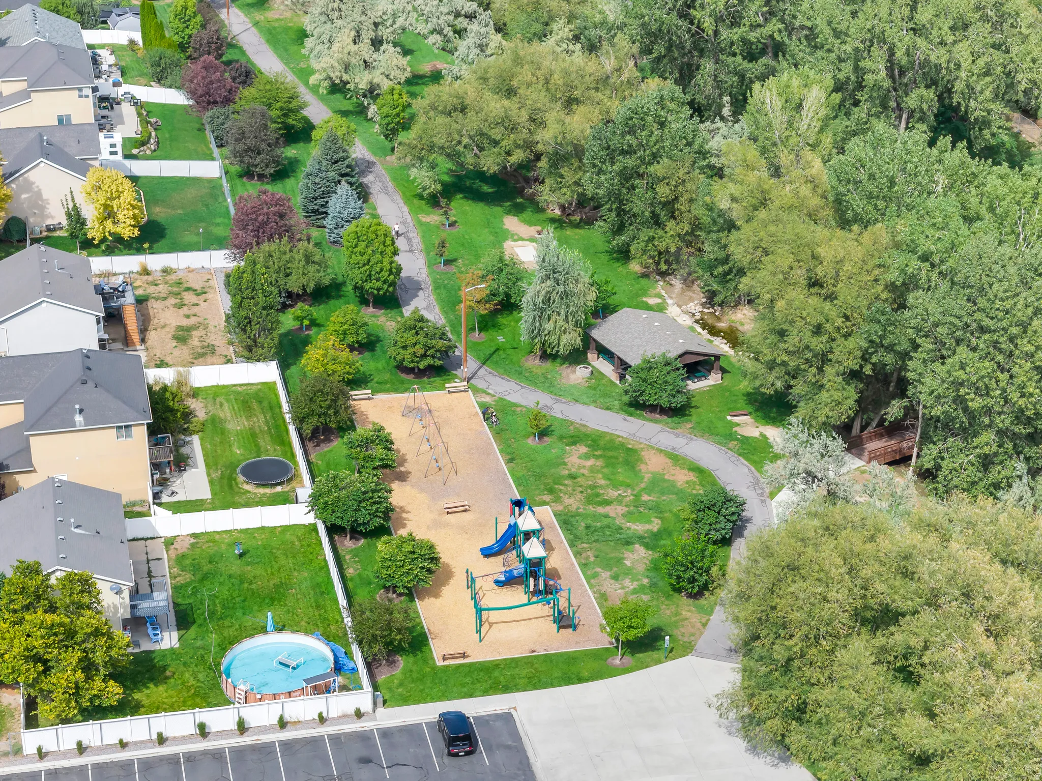 Neighborhood park with a children's playground, a paved walking path, and mature trees