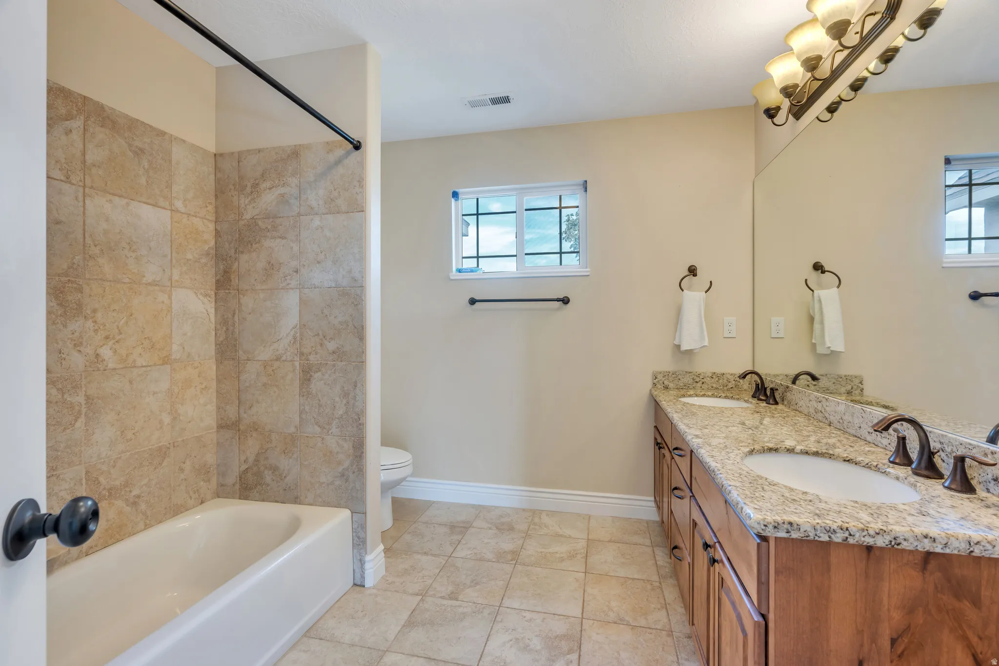 Dual vanity with stone countertop, wood-finish cabinetry, integrated sinks, and bronze-finish fixtures