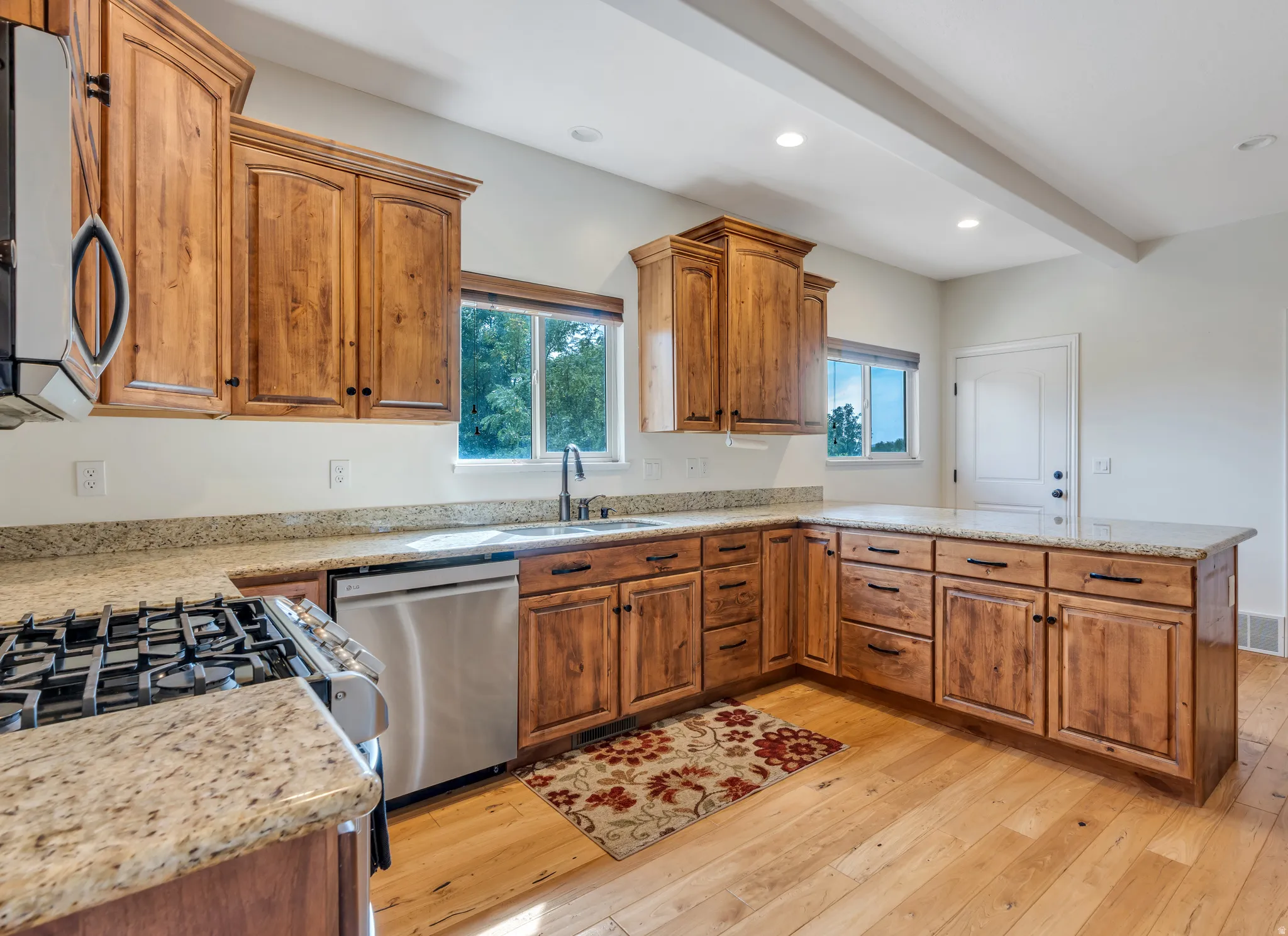 Kitchen featuring wood cabinetry, light-toned countertops, stainless steel appliances, and wood-finish flooring