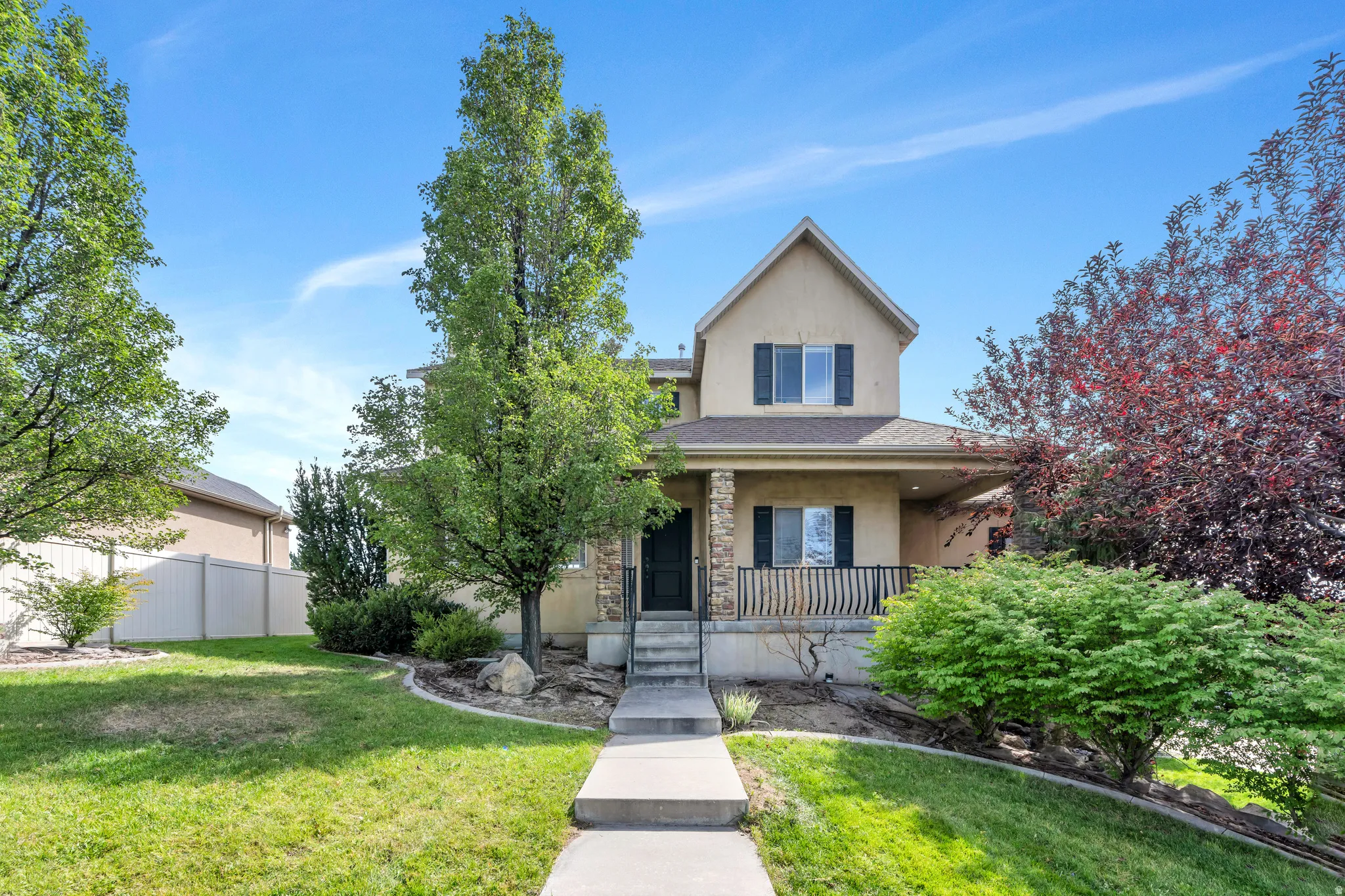 Two-story exterior with a covered front porch, stone column accents, dark window shutters, and a concrete pathway leading to the entry