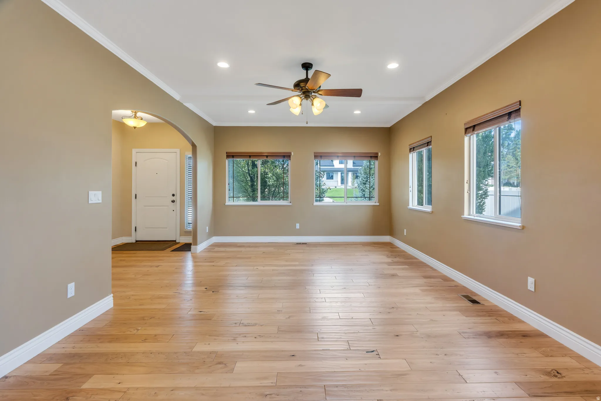 Wood-finish flooring, recessed lighting, crown molding, arched entry, and a ceiling fan