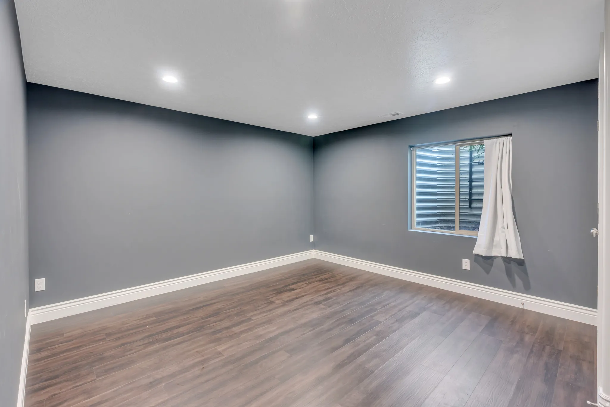 Recessed lighting illuminates this room featuring wood-finish flooring, a window with a window well, and crisp white trim