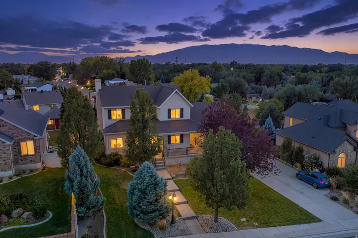 Two-story residence with a covered porch, established trees, and a concrete driveway, twilight added