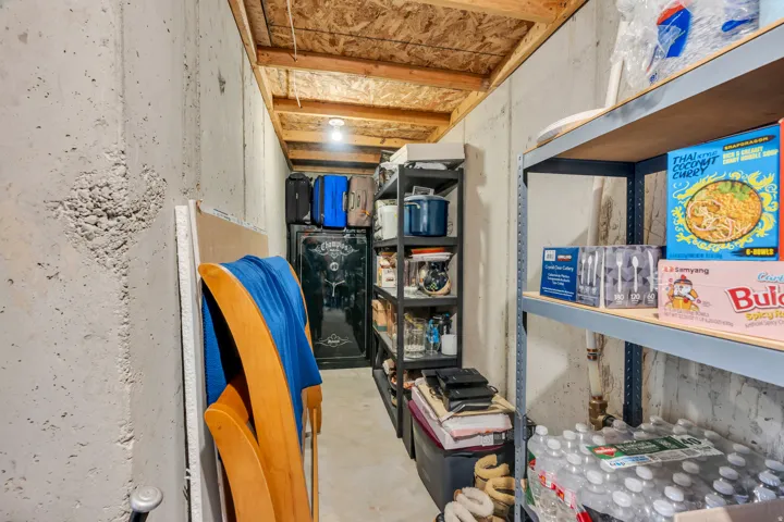 Unfinished space featuring exposed concrete walls and ceiling joists, with a light fixture and permanent shelving