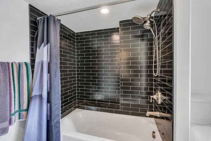 Bathtub with dark subway tile surround, built-in shower niche, and brushed nickel fixtures