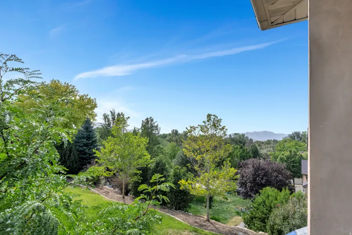 Lush landscaping with mature trees, sloped grassy areas, and distant mountain scenery