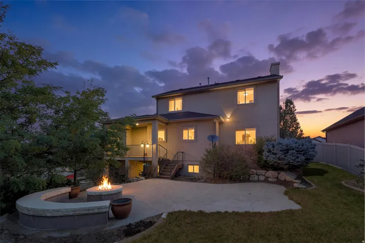 Rear exterior showcasing a built-in fire pit with stone seating, concrete patio, and a covered balcony, twilight added