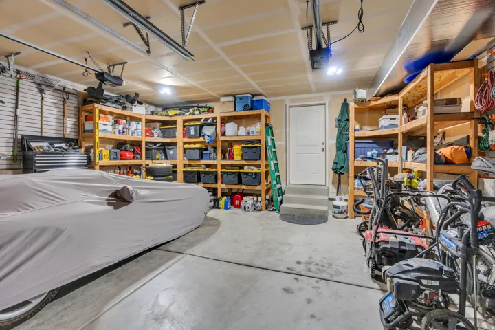 Spacious garage featuring epoxy-coated concrete flooring, custom wooden shelving with ample storage capacity, recessed and pendant lighting throughout, a white service door, and organized workspace ideal for hobbies, projects, or vehicle storage