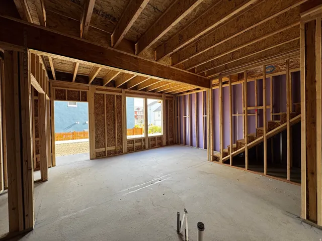 Unfinished interior showcasing structural wood framing, visible ceiling joists, concrete flooring, multiple window openings, and a framed staircase