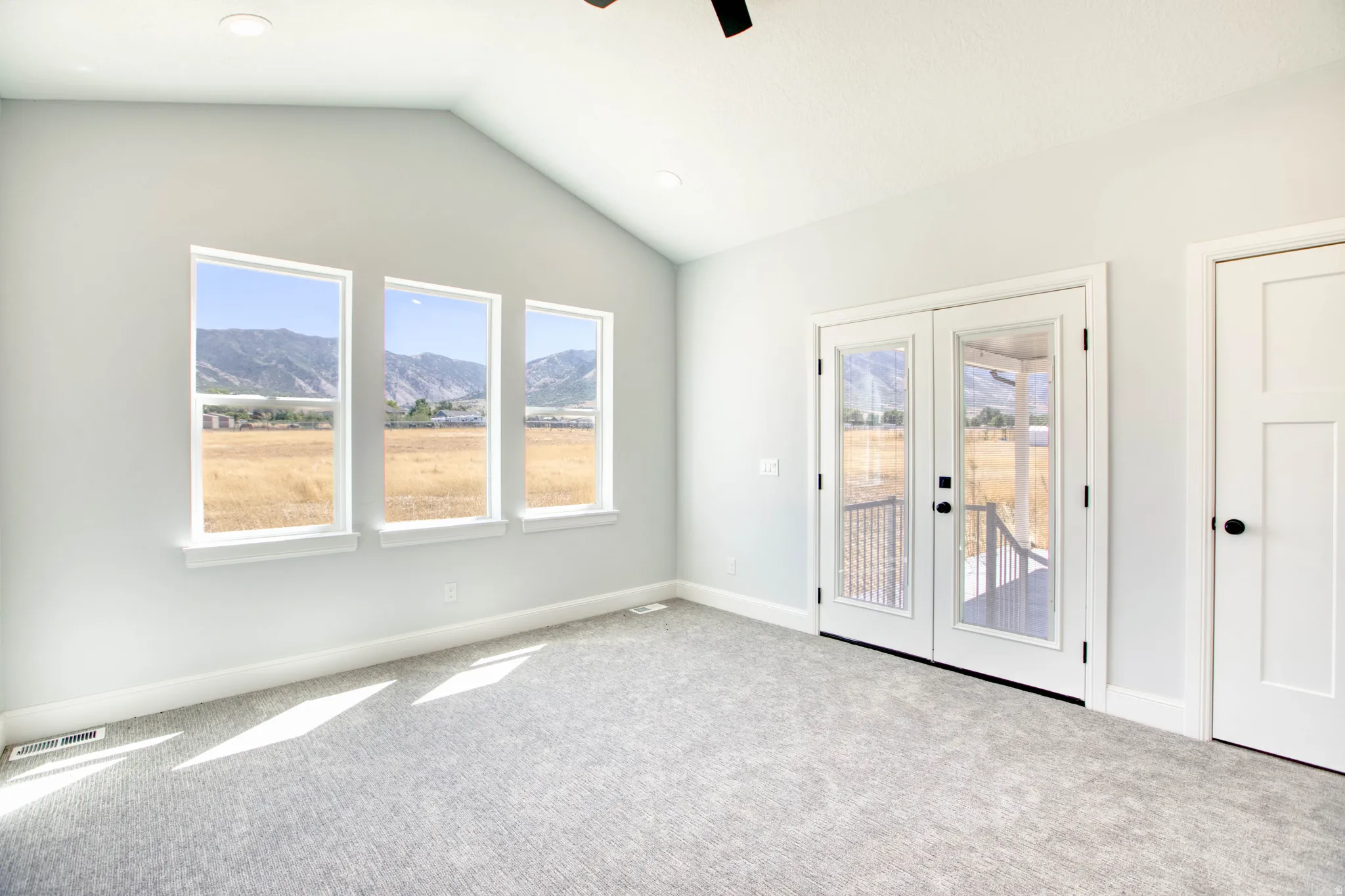Vaulted ceiling, recessed lighting, three large windows, double glass panel doors, and neutral carpet