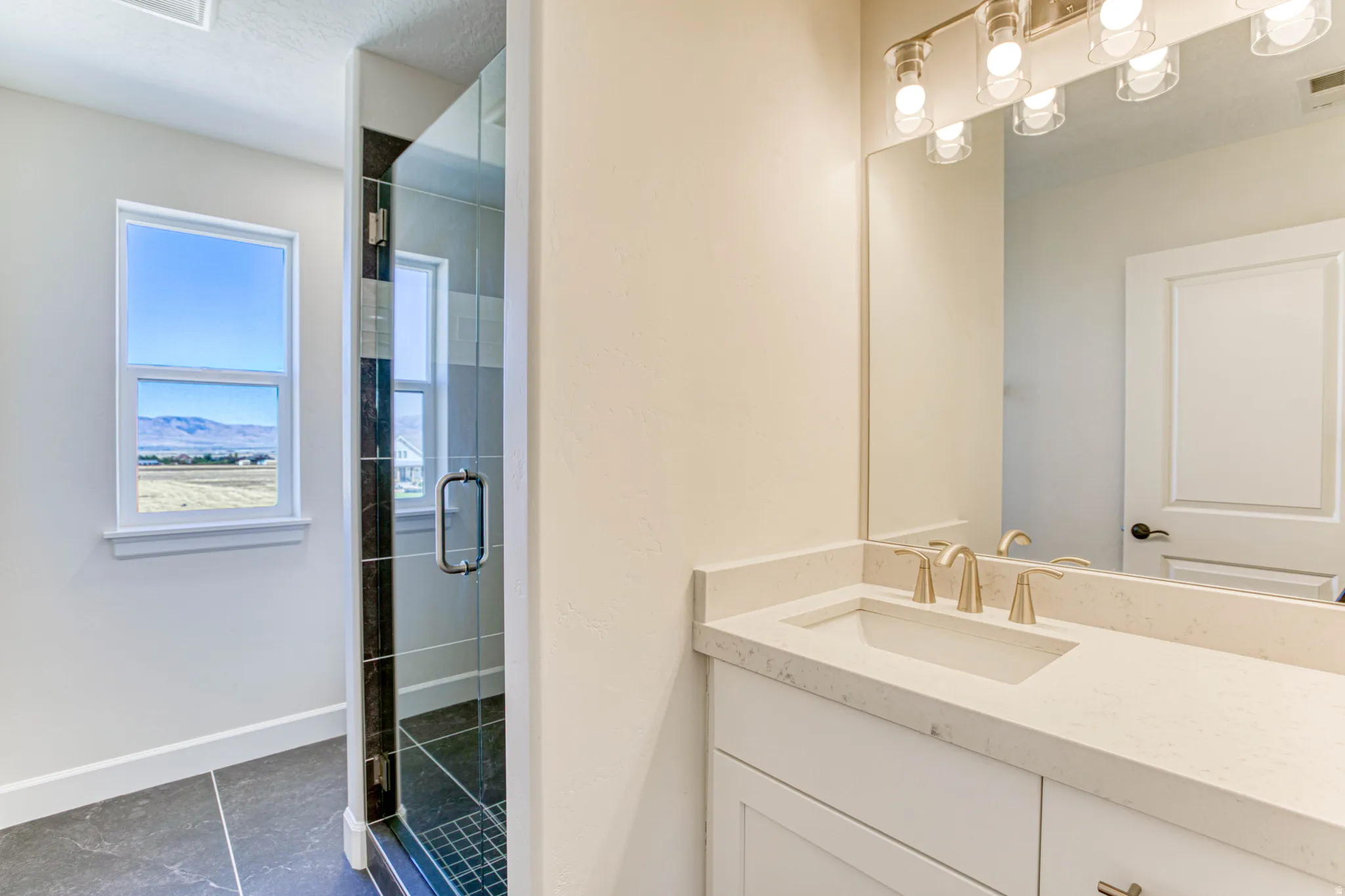 White vanity with a light-colored countertop and undermount sink, brushed nickel faucet, frameless mirror, and overhead vanity lighting