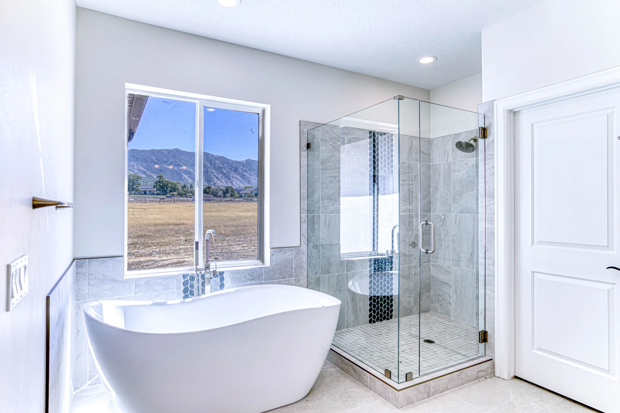 Freestanding soaking tub with a floor-mounted faucet, glass-enclosed shower, large format tiled walls, and a recessed ceiling light