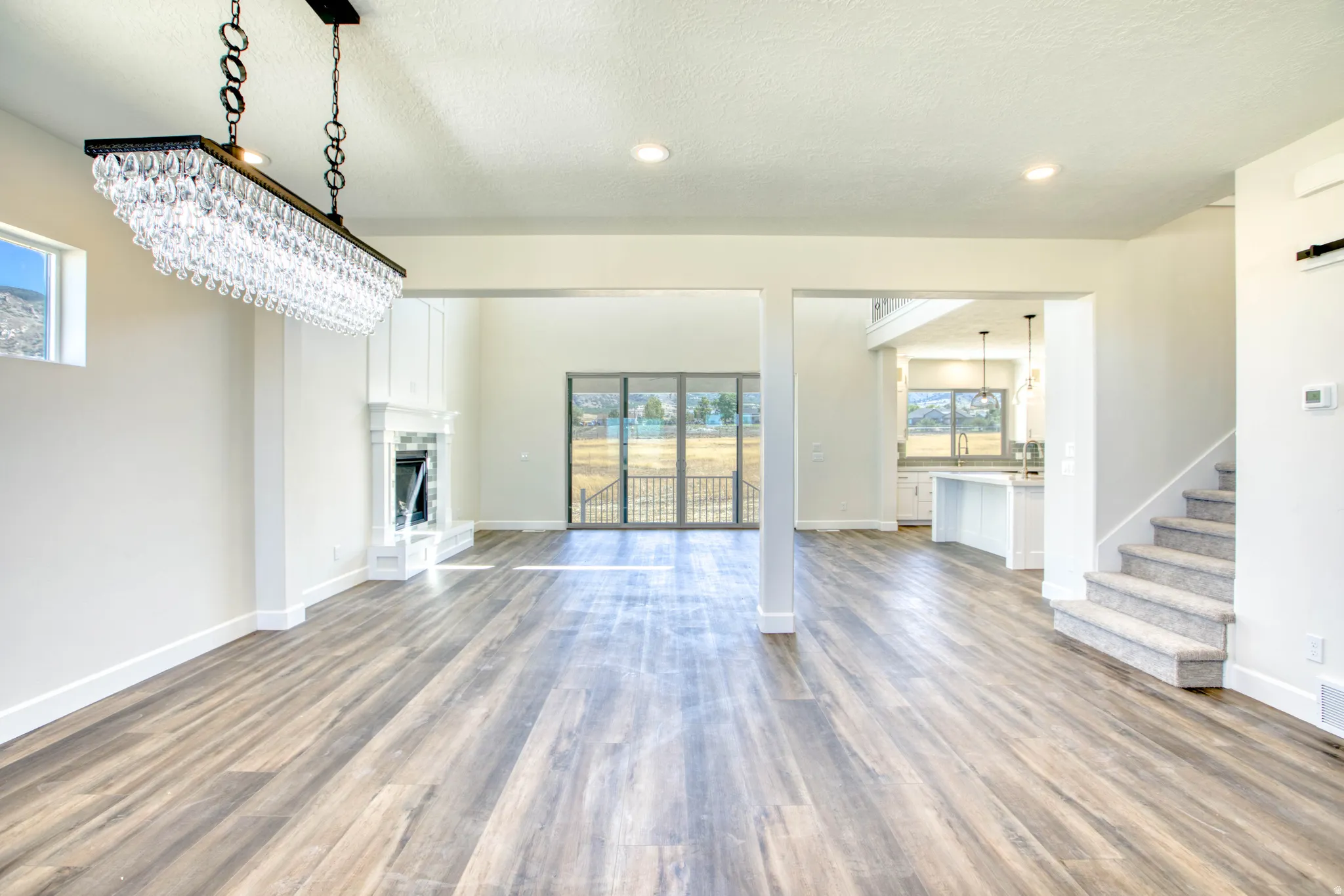 Spacious interior with wood-finish flooring, a white mantel fireplace, and a crystal chandelier