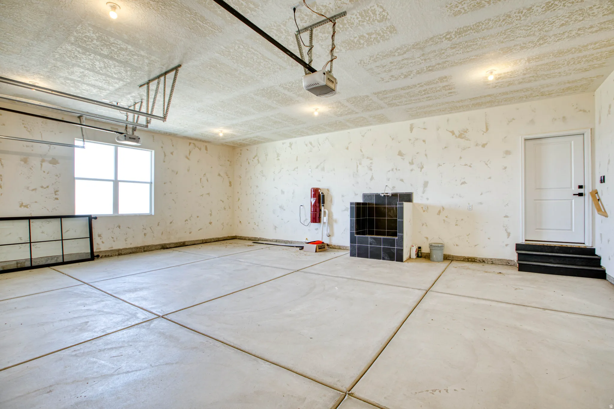 Spacious garage featuring a window, built-in black tiled utility sink, concrete flooring, and a service door