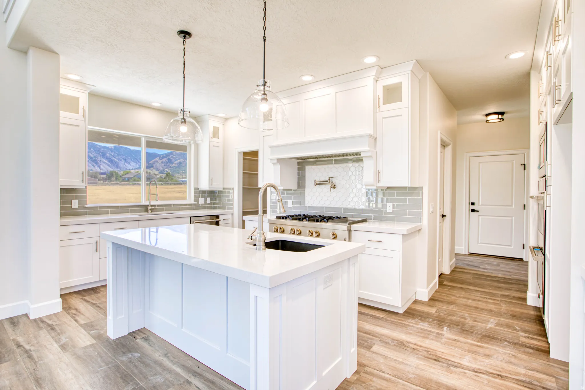 Kitchen featuring an expansive center island with an integrated sink, white cabinetry, integrated stainless steel appliances, and wood-finish flooring