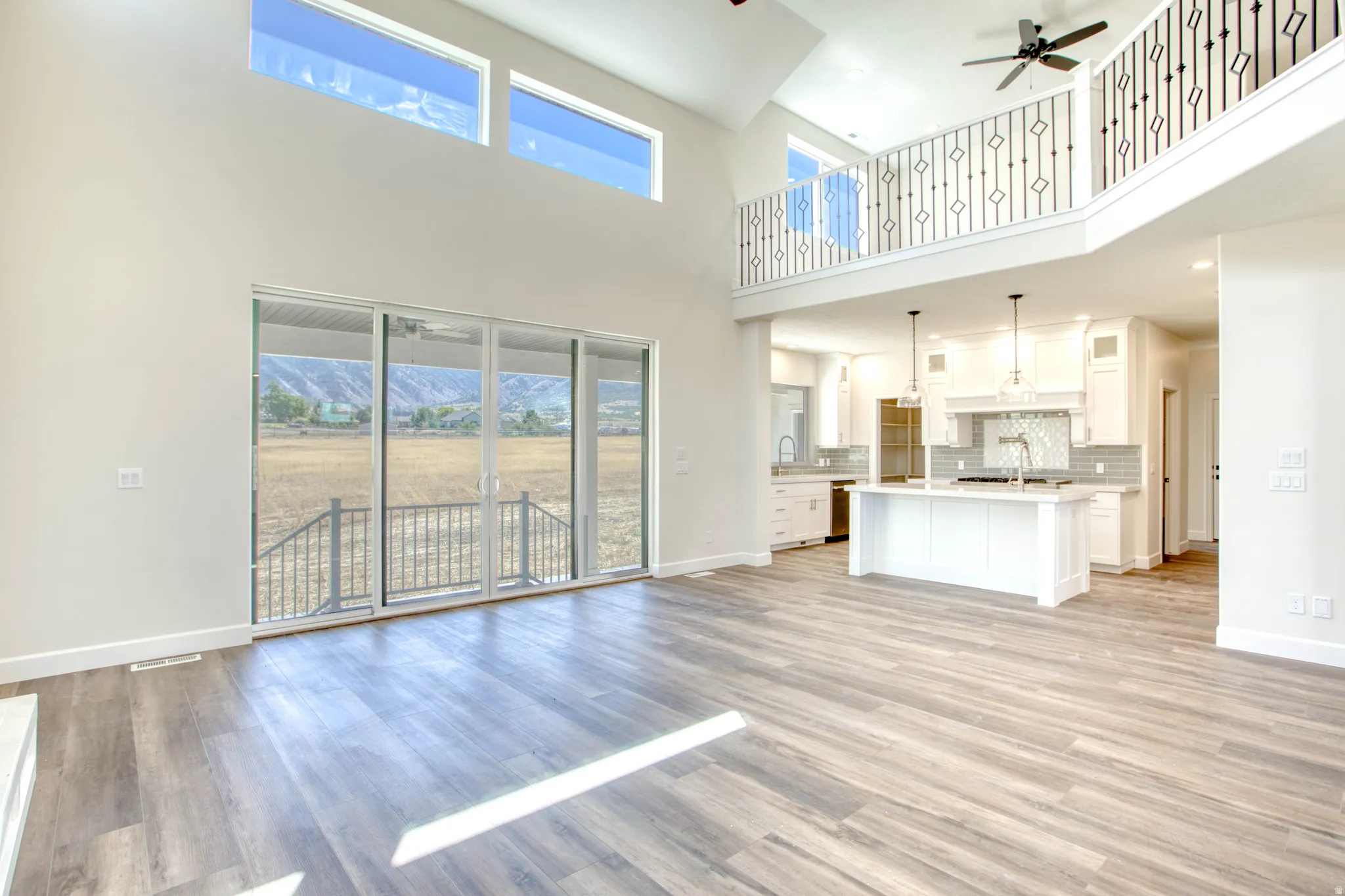 Vaulted ceilings, wood-finish flooring, sliding glass doors, white kitchen cabinetry, and a kitchen island with pendant lighting