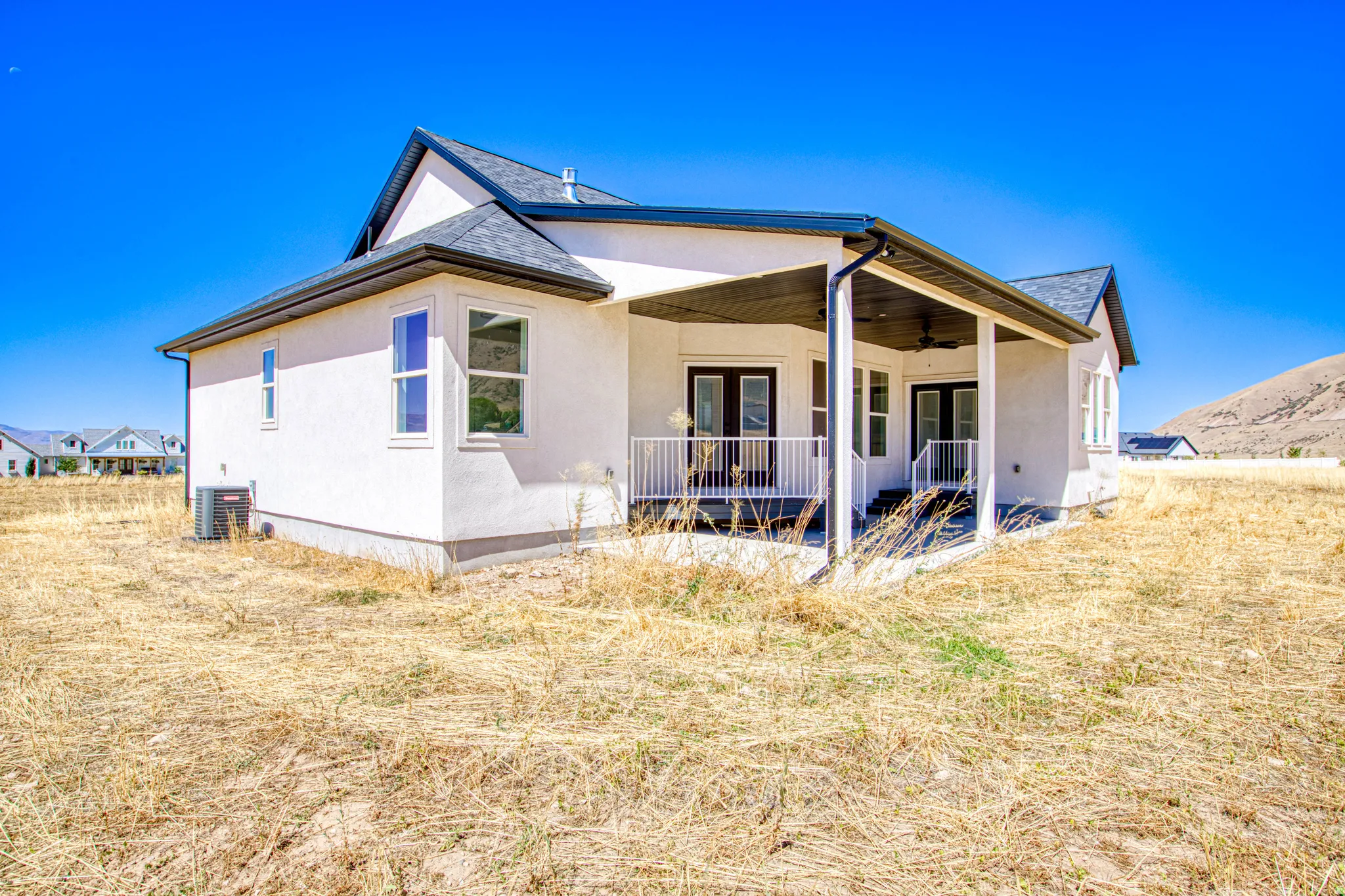 Stucco exterior with a covered patio, dark roofing, white window frames, and a white railing