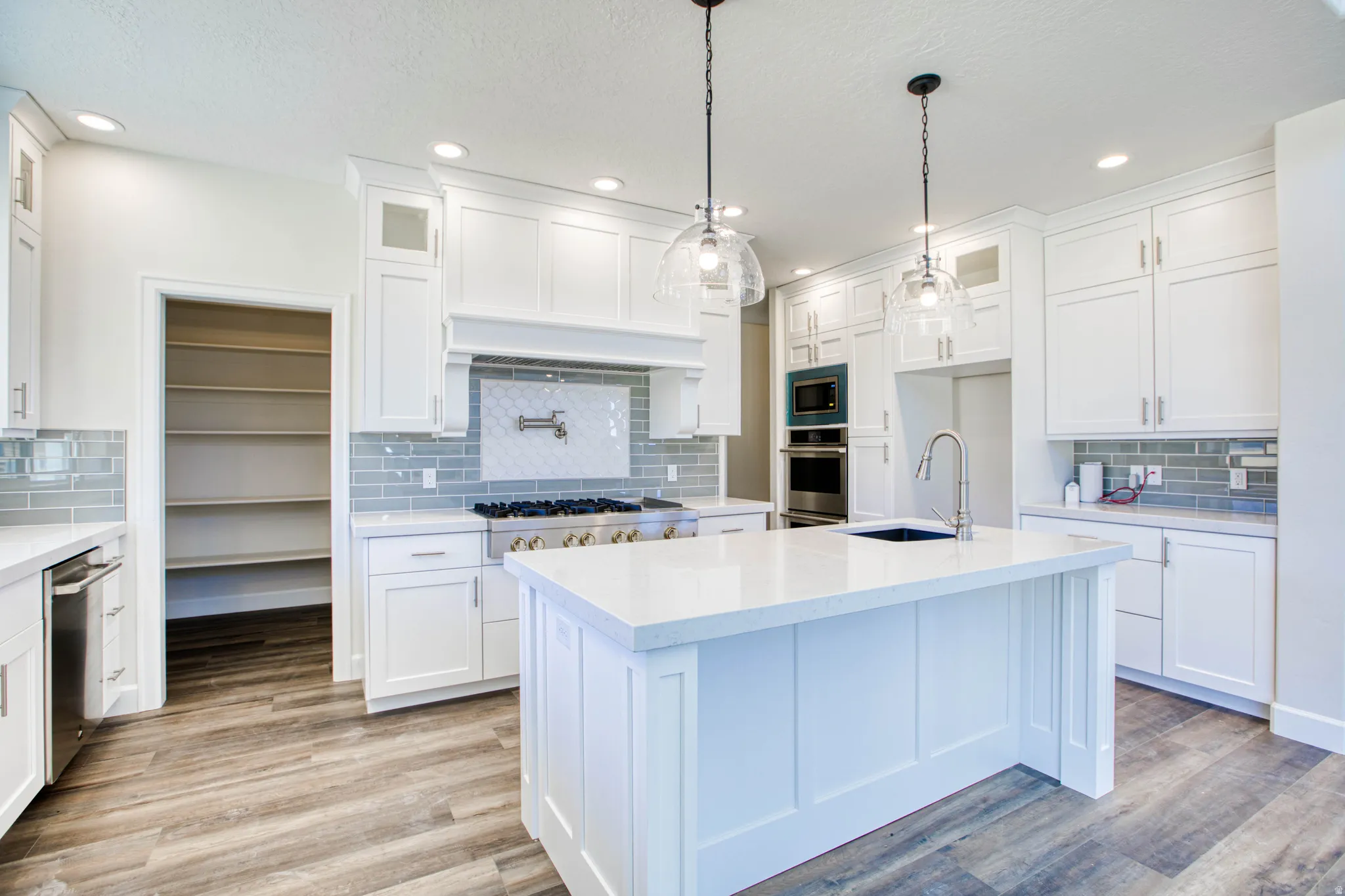 Modern kitchen featuring white cabinetry, light-colored countertops, a tile backsplash, wood-finish flooring, and pendant lighting
