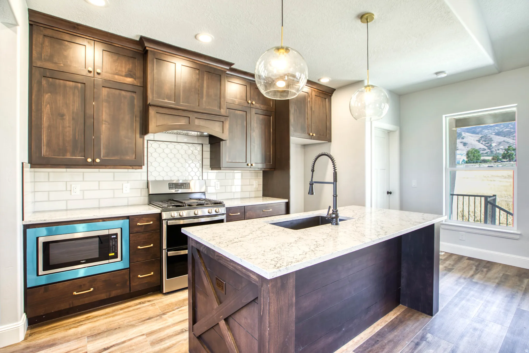 Dark wood-finish cabinetry, light-toned countertops, stainless steel appliances, a center island with a sink, and wood-finish flooring