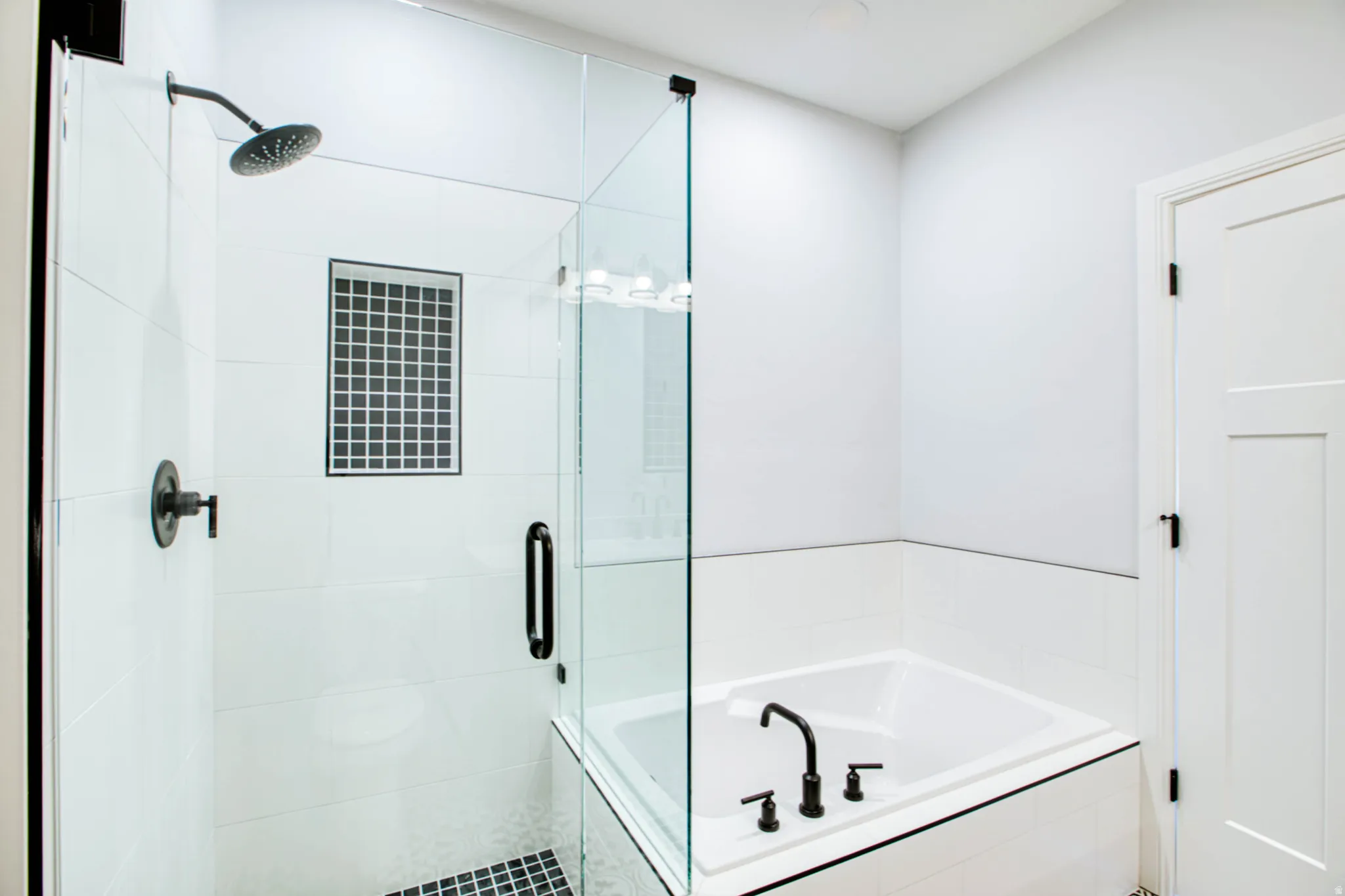 Glass-enclosed shower with matte black fixtures, white subway tile surround, and a recessed niche