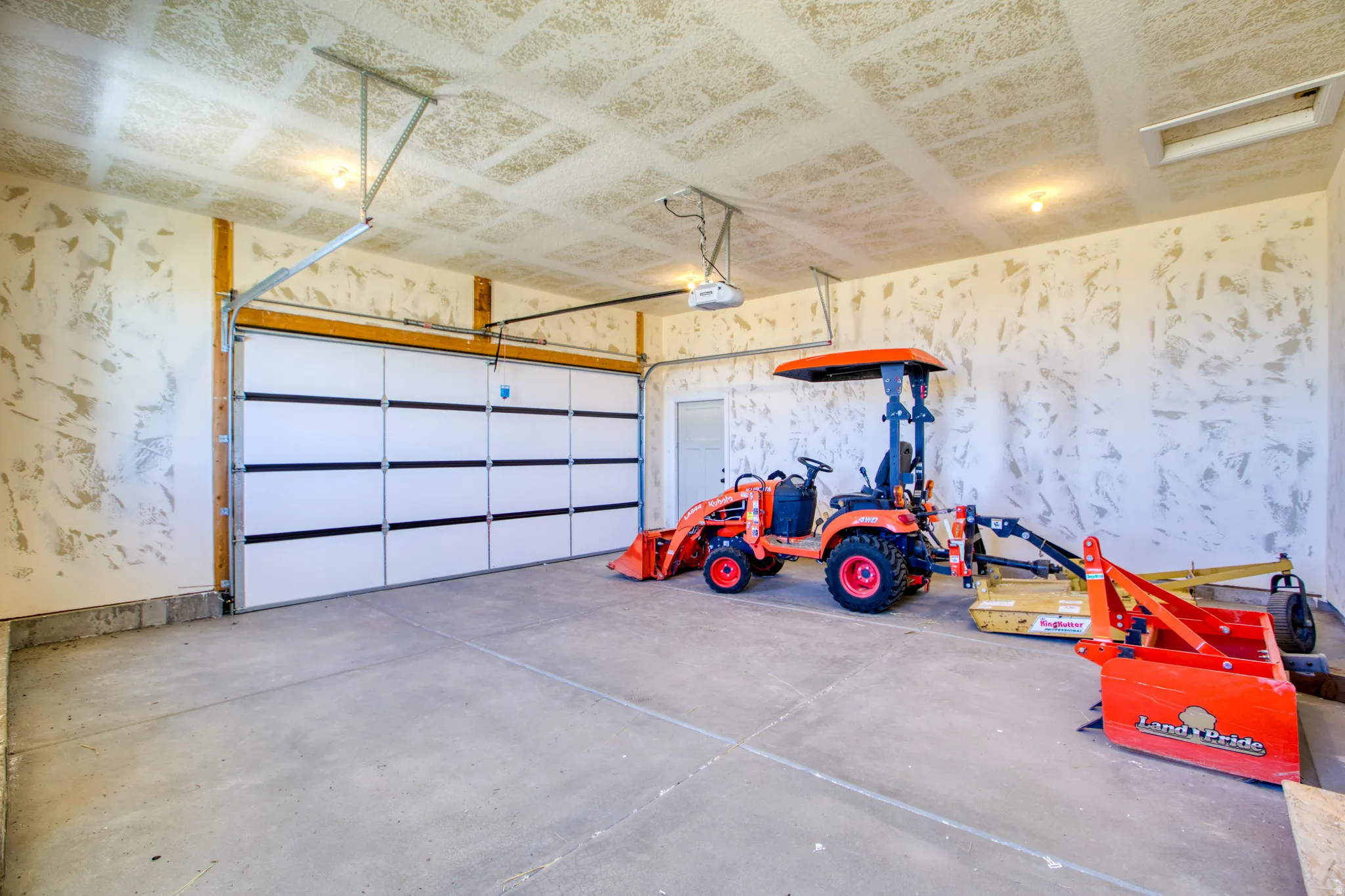 Concrete flooring with a white paneled garage door, exposed wood beams, and a side entry door