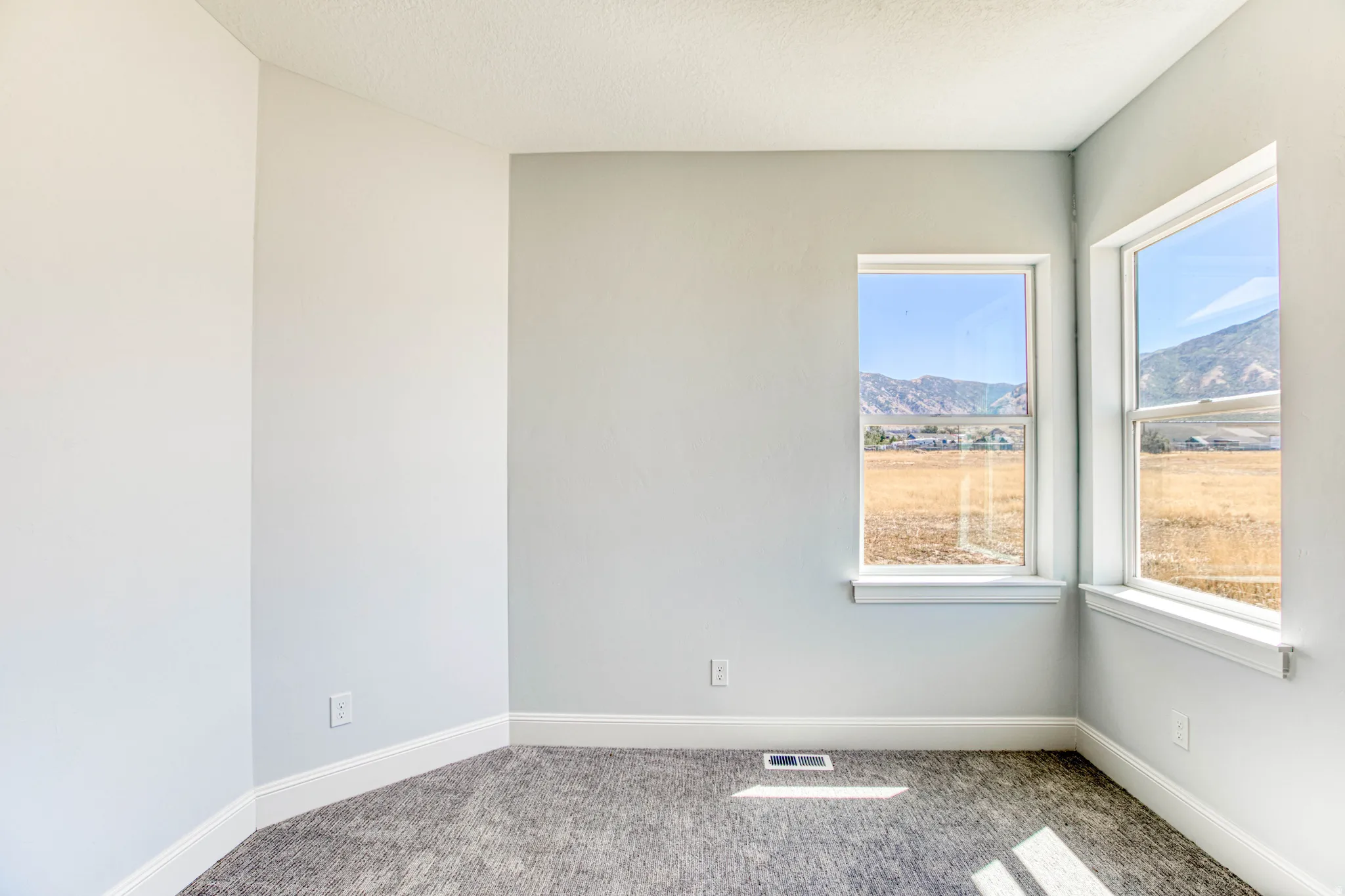 Corner windows with white trim, light gray painted walls, and textured carpeting